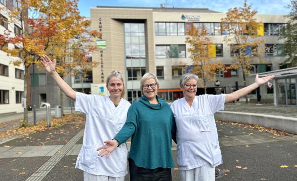 Tre kvinner mer armene i været på åpen plass foran bygning