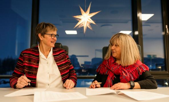 To kvinner som signerer en avtale i et opplyst rom ved et vindu og under en julestjerne. Foto