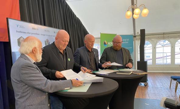 Fire menn rundt to bord som signerer papirer. Foto
