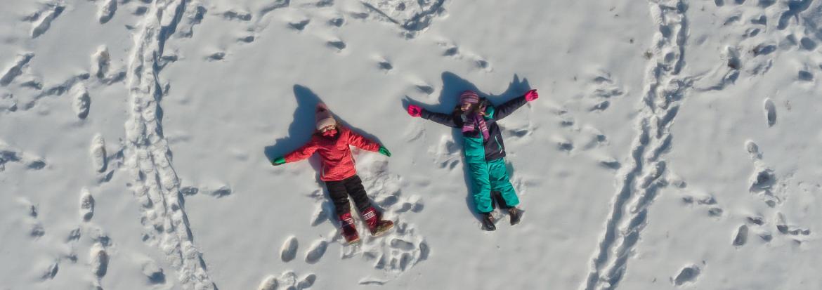 To barn som ligger i snøen sett fra lufta. Barna ligger inne i et stort opptråkka hjertemønster.