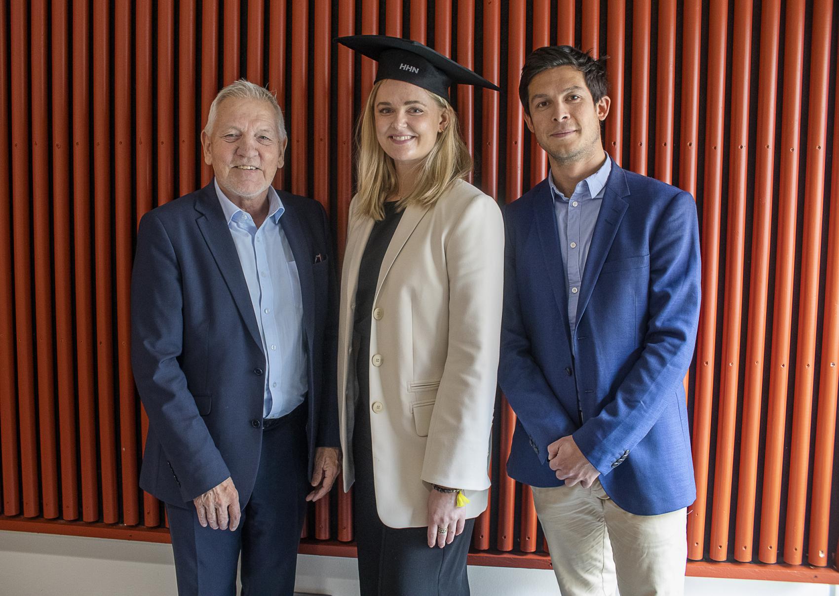A female student, with a graduation hat, stands between two men in a posed picture. 