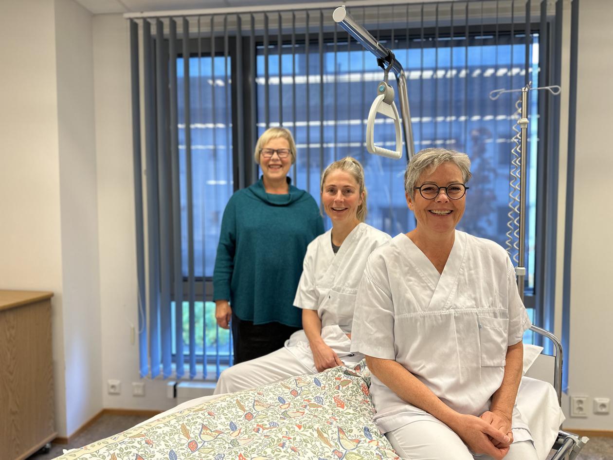 Tre kvinner som sitter på sykeseng, smiler og ser i kamera